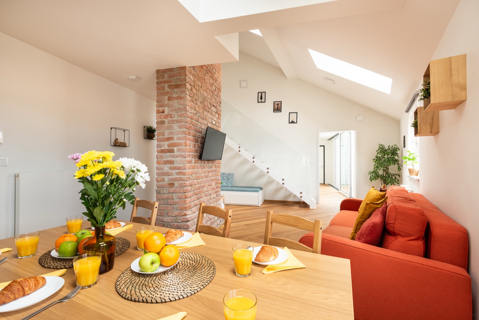 Prosvětlený obývací prostor apartmánu v Řehořově s jídelním stolem, cihlovým pilířem a oranžovou pohovkou